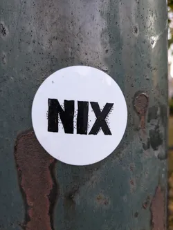 Street sticker A round white sticker with the word NIX written in bold, black, stylized lettering. The sticker is affixed to a weathered, dark teal metal pole.