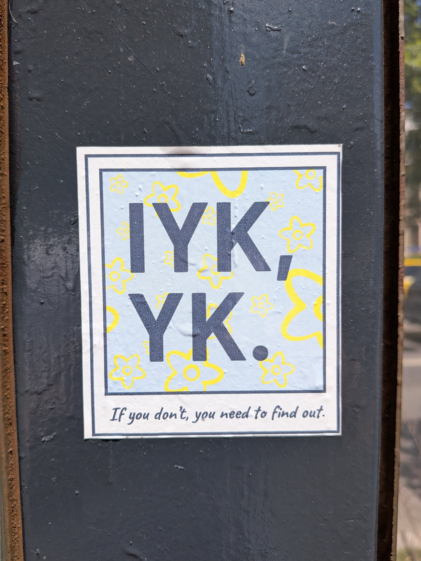 A square sticker designed like a Polaroid photo. The central image has a light blue background patterned with yellow outline flowers. Large, dark grey letters spell 'IYK, YK.' across the center. The bottom white border features the handwritten text, 'If you don't, you need to find out.'