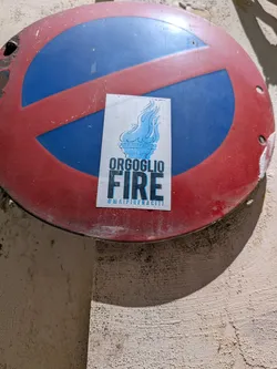 Street sticker Rectangular white sticker depicting a blue flame torch. Below the graphic, the text reads 'ORGOGLIO FIRE' in bold black and blue fonts, with the hashtag '#MAIPIUFRACITI' at the bottom.