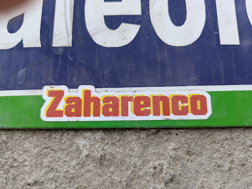 A sticker that says 'Zaharenco' in red with a yellow border on a white background. The sticker is placed on a green and blue sign.