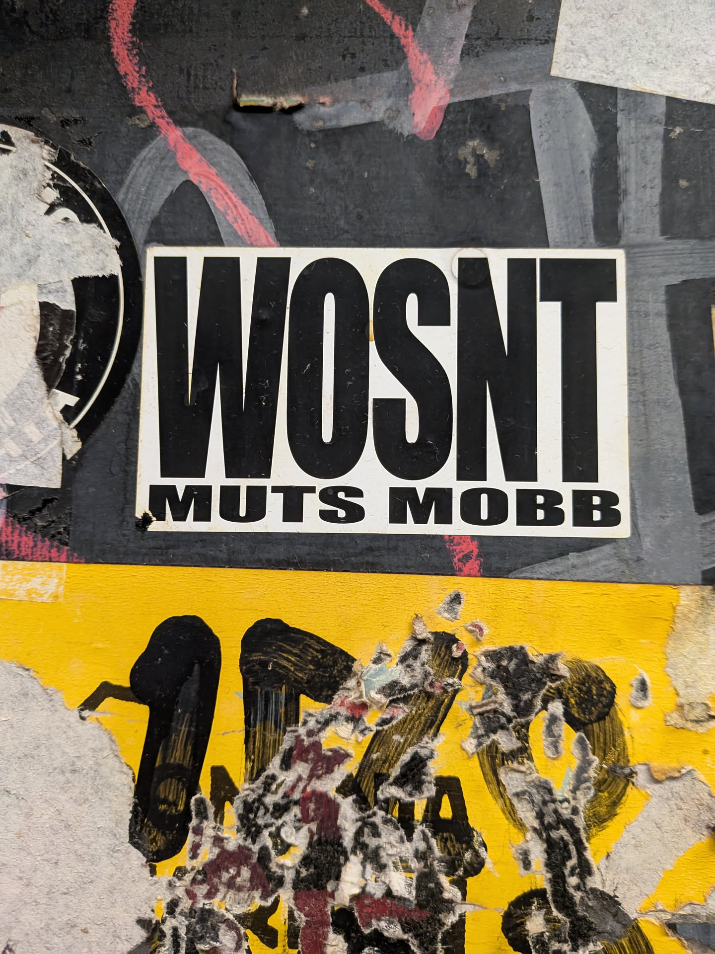 A rectangular white sticker featuring bold black typography. The top line reads 'WOSNT' in tall, condensed letters, while the bottom line reads 'MUTS MOBB' in a wider, smaller font.