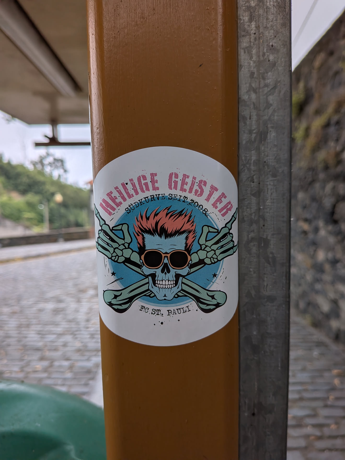 Circular sticker depicting a blue skull with spiky orange hair and sunglasses. Behind it are crossed green bones with hands making the 'rock on' sign. Text reads 'HEILIGE GEISTER', 'SÜDKURVE SEIT 2008', and 'FC ST. PAULI'.
