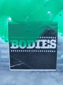 Street sticker A dark teal square sticker with the word BODIES in a bold, sans-serif font. The word is surrounded by a row of small white stars at the top and bottom. The sticker appears to be slightly damaged or worn.