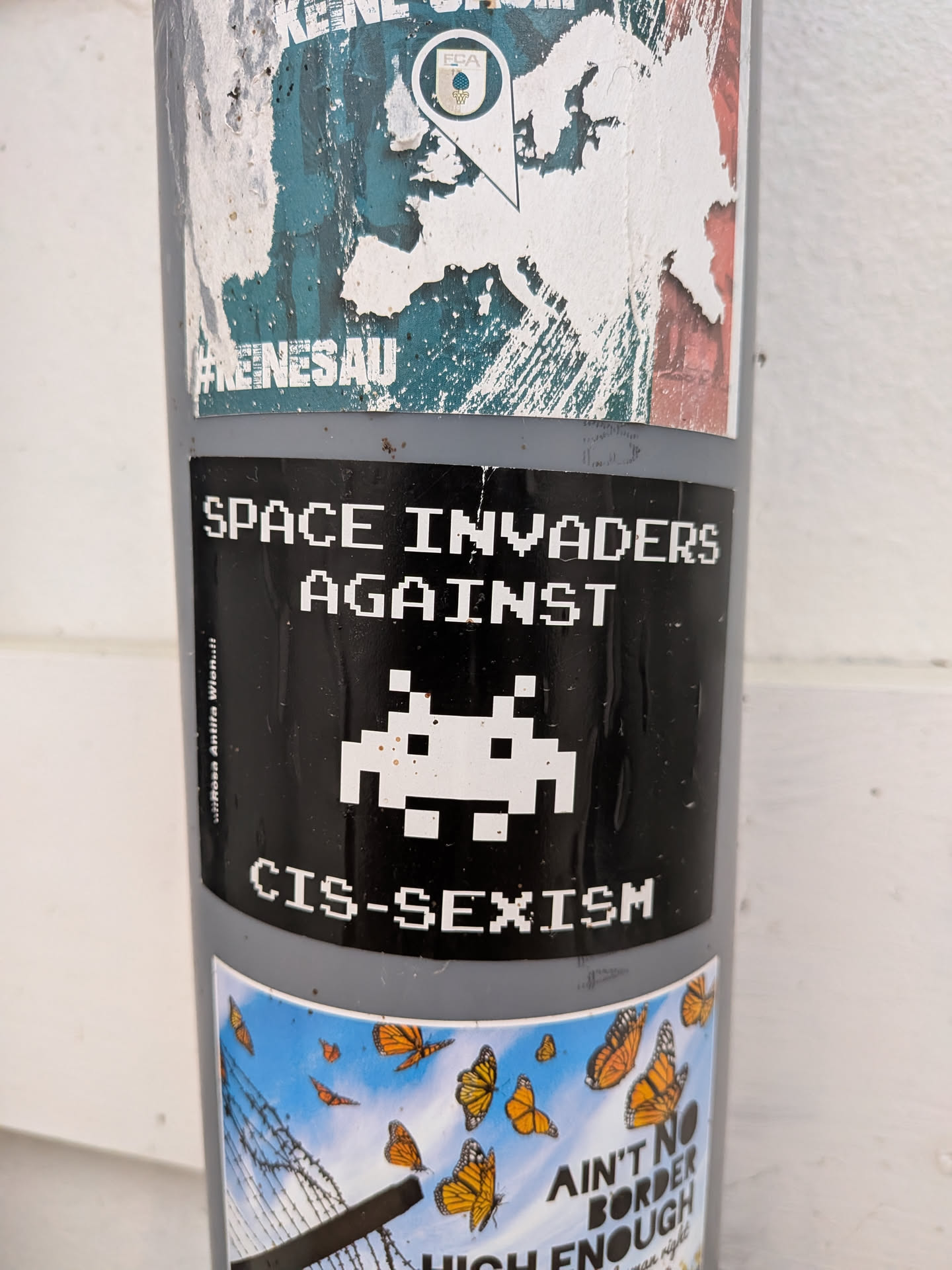 Black rectangular sticker with white pixel art. Features a Space Invader alien between the text 'SPACE INVADERS AGAINST CIS-SEXISM'. Small vertical text on the left reads ':::Rosa Antifa Wien.::'.