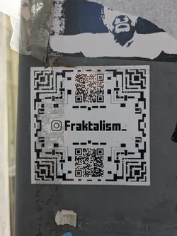 Street sticker This is a sticker featuring a complex design primarily consisting of QR code patterns around the edges and center. An Instagram handle, @Fraktalism_, is printed prominently in the middle. This sticker likely serves as a creative way to direct people to an online presence using a scannable QR code.