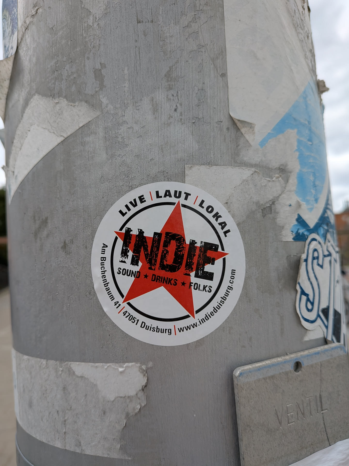 Circular white sticker featuring a central red star overlaid with the word 'INDIE' in distressed black font, surrounded by address and website details.