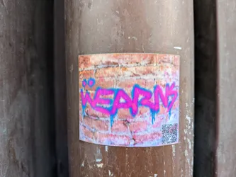 Street sticker The sticker features a stylized graffiti tag in vibrant neon pink with bright blue outlines and drips. The tag appears to be the word 'WEARNY'. The background of the sticker is designed to look like a brick wall, with varying shades of orange, pink, and brown bricks. A QR code is visible in the bottom right corner of the sticker.