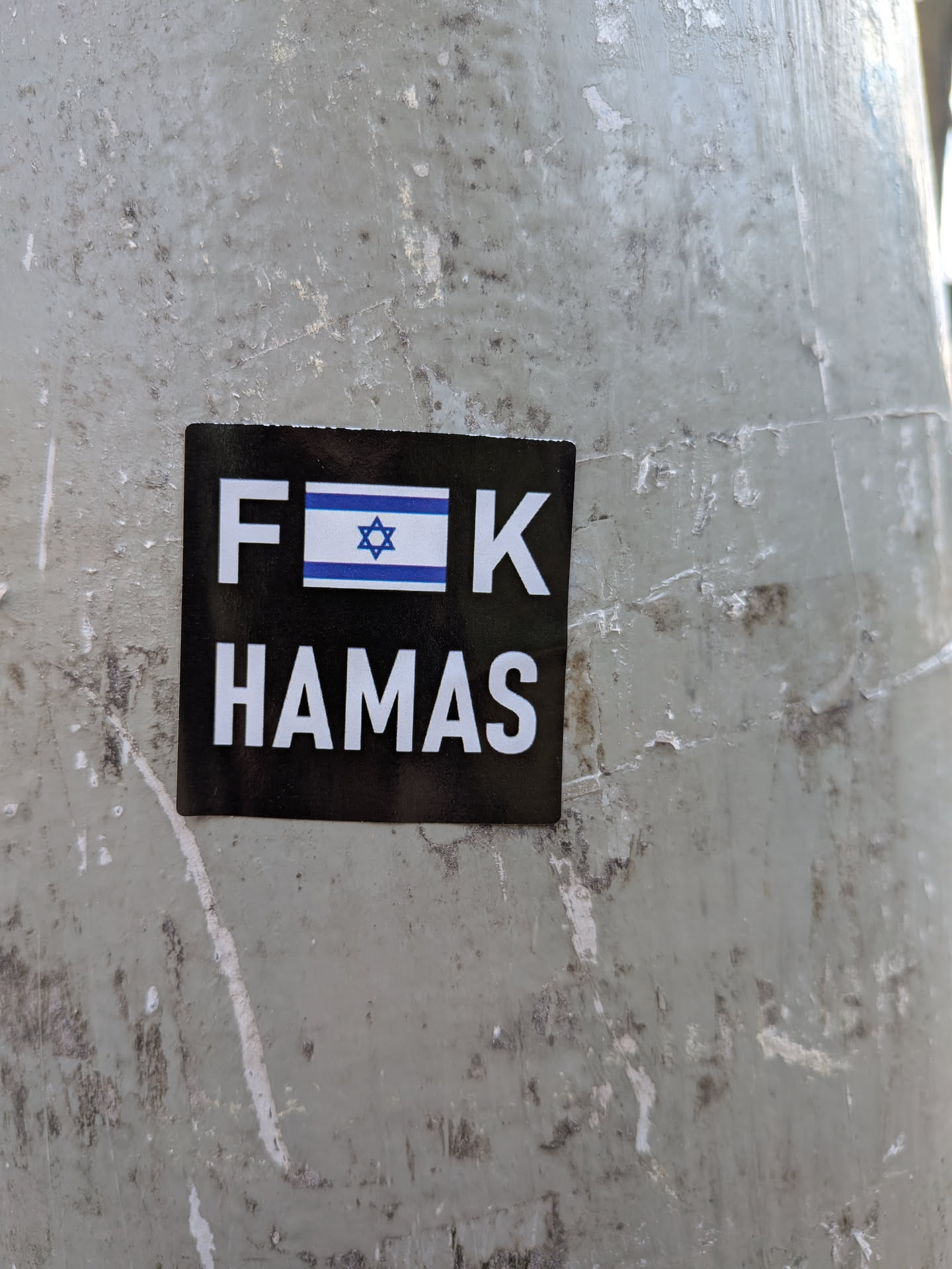 The sticker is black with white text and an image of the Israeli flag. The top line of text reads 'F' followed by the Israeli flag, and then 'K'. The second line of text reads 'HAMAS' in all capital letters. The sticker appears to be adhered to a weathered, grey surface.