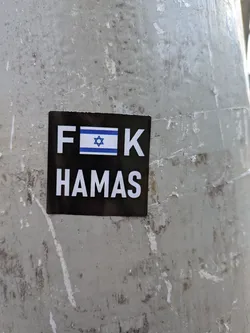 Street sticker The sticker is black with white text and an image of the Israeli flag. The top line of text reads 'F' followed by the Israeli flag, and then 'K'. The second line of text reads 'HAMAS' in all capital letters. The sticker appears to be adhered to a weathered, grey surface.