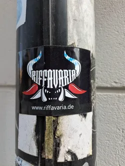 Street sticker This sticker features the stylized text 'RIFFAVARIA' above a monster-like face with horns that resemble the Bavarian flag pattern. The URL www.riffavaria.de is printed below the design. The sticker is affixed to a pole.
