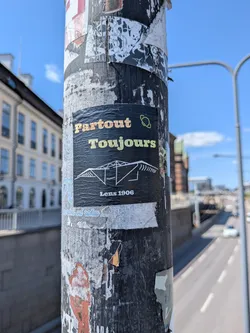 Street sticker A black rectangular sticker featuring the text 'Partout Toujours' in orange and yellow, a white line drawing of a stadium roof, and 'Lens 1906' at the bottom.