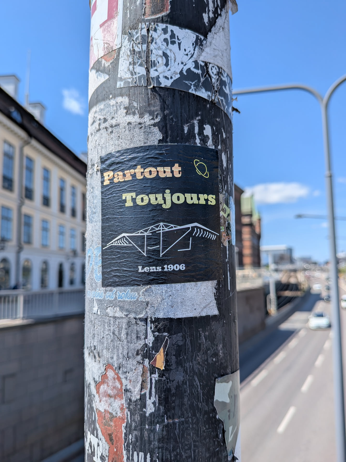 A black rectangular sticker featuring the text 'Partout Toujours' in orange and yellow, a white line drawing of a stadium roof, and 'Lens 1906' at the bottom.