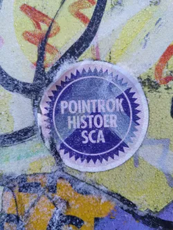 Street sticker A purple and pink sticker with the text "Pointrok Histoer SCA" on it. The sticker is attached to a wall with other graffiti and covered in a layer of what looks like snow or frost.