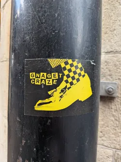 Street sticker A rectangular black sticker depicting a yellow graphic of a foot wearing a tasseled loafer, checkered socks, and houndstooth trousers. The text 'GNAGET CRAZE' is displayed in blocky yellow letters on the left.