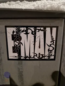 Street sticker A black and white sticker with the word 'EMA' in bold, uppercase letters.  The lettering is framed by a decorative, tribal-style design. The sticker has a slightly grungy, graffiti-like aesthetic.