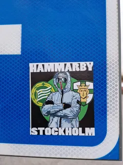 Street sticker A sticker featuring a stylized illustration of a person wearing a hooded jacket, with the words "HAMMARBY" and "STOCKHOLM" at the top and bottom, respectively.  The image is set against a background that includes a crest or logo.