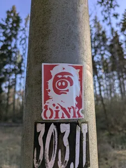 Street sticker The sticker shows a pig's head wearing a revolutionary style hat with a red star. Below the pig is the text "OINK" also in red. The sticker is on a concrete pole.
