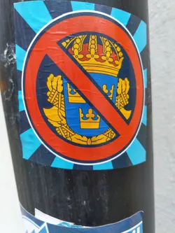 A sticker with a red circle and a diagonal line over a coat of arms, likely expressing anti-monarchist sentiment.