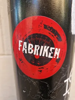 Red and black circular sticker with a gauge and the word Fabriken. Made in Sweden is also visible.