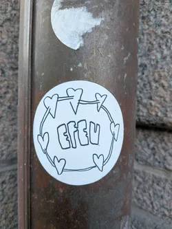 Street sticker The sticker is circular with a white background, featuring a simple, hand-drawn design in black outline. A thin line connects several small, stylized hearts around the perimeter, forming a circular frame. Inside this frame, the word "EFEU" is written in a bold, bubble-letter style, also in black outline. The overall aesthetic is minimalist and doodle-like.