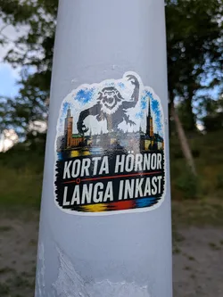 Street sticker Die-cut sticker showing a giant ape towering over Stockholm's skyline. Below, the Swedish text 'KORTA HÖRNOR LÅNGA INKAST' is printed in white on a black background, accented by a red line and Swedish flag colors at the bottom.