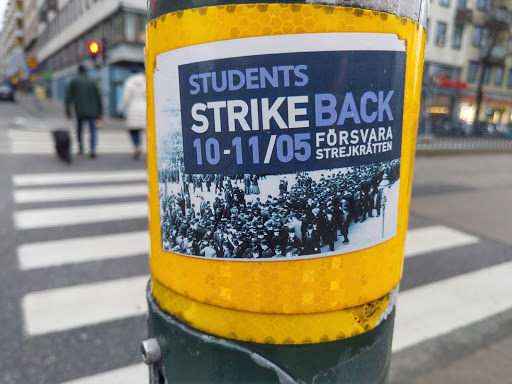 Street sticker A sticker featuring a black and white image of a large group of people, possibly a protest or demonstration.  The text on the sticker reads "STUDENTS STRIKE BACK 10-11/05 Försvara strejkrätten".  The sticker is affixed to a yellow pole.