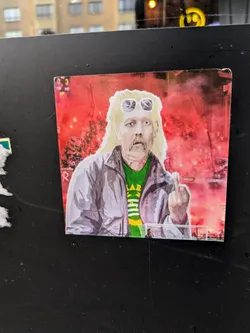 Street sticker This sticker features a stylized illustration of a man who seems to be a football fan, possibly at a match where flares are being lit.  He's sporting a mullet, sunglasses, and a green and yellow shirt, giving a middle finger gesture. The style is bold and slightly graphic. The background is a hazy red, possibly suggesting a nighttime setting or the smoky atmosphere of a stadium. 