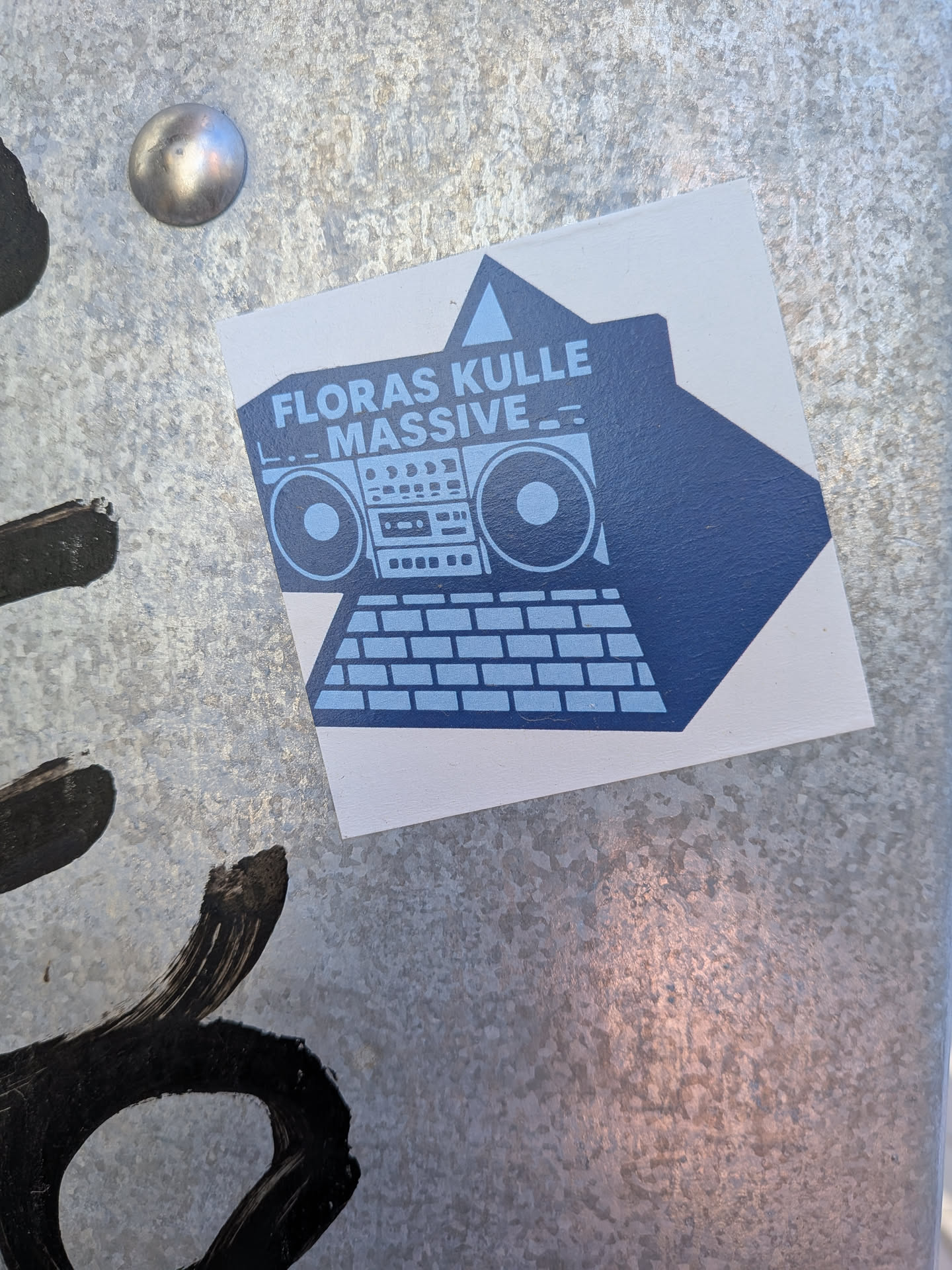 The sticker is a roughly square-shaped decal with a white background, featuring a two-tone blue graphic. The central image is a stylized, retro boombox rendered in a dark blue silhouette, with internal details like speakers, buttons, and a cassette deck area highlighted in a lighter blue. Above the boombox, the text "FLORAS KULLE MASSIVE" is prominently displayed in a blocky, light blue font. The overall aesthetic is clean, graphic, and reminiscent of old-school music culture.
