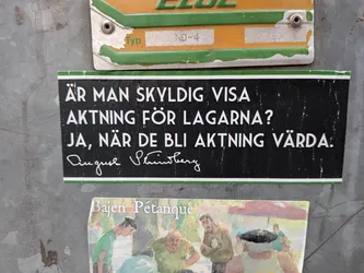 Street sticker A rectangular sticker with a black background and thin green borders at the top and bottom. It features white, capitalized sans-serif text in Swedish posing a question and answer about the obligation to respect laws. Below the text is the white signature of the famous Swedish writer August Strindberg. The sticker is affixed to a scratched, grey metal surface.