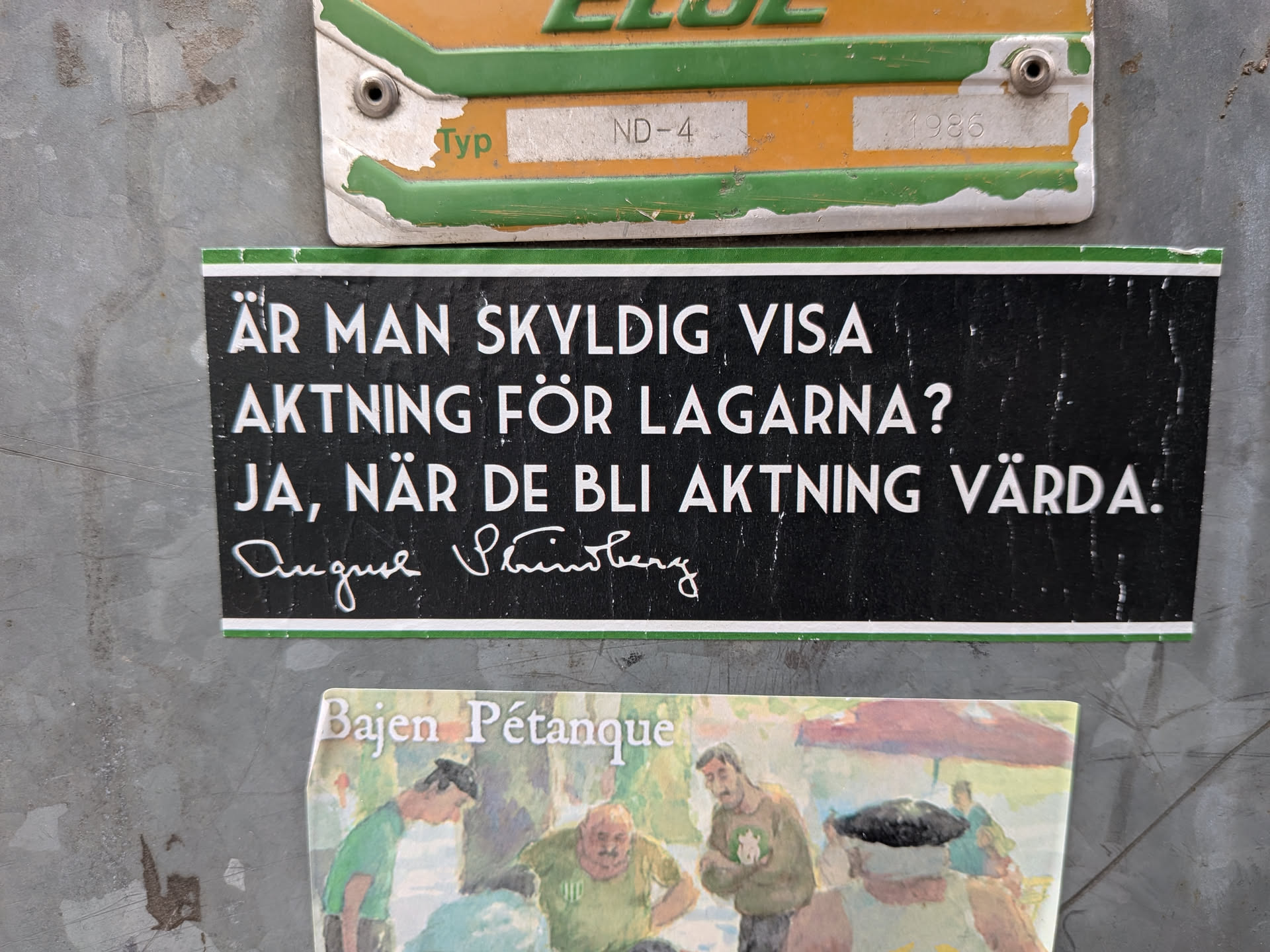 A rectangular sticker with a black background and thin green borders at the top and bottom. It features white, capitalized sans-serif text in Swedish posing a question and answer about the obligation to respect laws. Below the text is the white signature of the famous Swedish writer August Strindberg. The sticker is affixed to a scratched, grey metal surface.