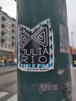 A sticker with a black and white design and blue accents. It has the name "Julia Rio" written in the center. The bottom of the sticker shows a social media handle and a hashtag.