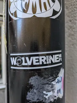 Street sticker A black and white sticker with the text "WOLVERINE HI-FI" in a bold sans-serif font. A small circle with a vinyl record icon is placed before the text. The sticker is affixed to a black pole.