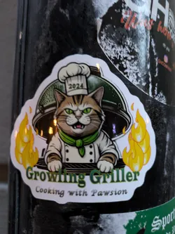 Street sticker The sticker features a cartoon cat dressed as a chef, complete with a white chef's hat and coat, and a green scarf. The cat has a grumpy expression with green eyes and is standing in front of a grill. Flames are depicted on either side of the cat, suggesting it is actively grilling. The year '2024' is visible on the chef's hat. Below the cat and grill, the text 'Growling Griller' is written in a bold, green, slightly stylized font, and beneath that, 'Cooking with Pawsion' is written in a more delicate, cursive font. The overall design has a humorous and playful aesthetic, with a white border around the sticker.