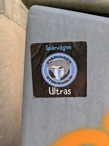 Street sticker The sticker is black with a blue and white round logo in the middle. The logo features a masked figure with the Swedish flag colors. The text reads "Spårvägen Stockholm Ultras".