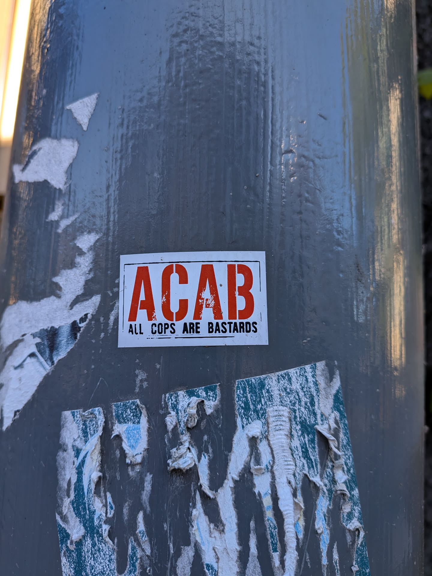 A rectangular sticker with a white background and a thin black border. The dominant text 'ACAB' is rendered in large, distressed, sans-serif red capital letters. Below this, in smaller, black, sans-serif capital letters, is the full phrase 'ALL COPS ARE BASTARDS'. The sticker shows minor signs of wear, particularly within the red lettering, giving it a slightly gritty appearance.