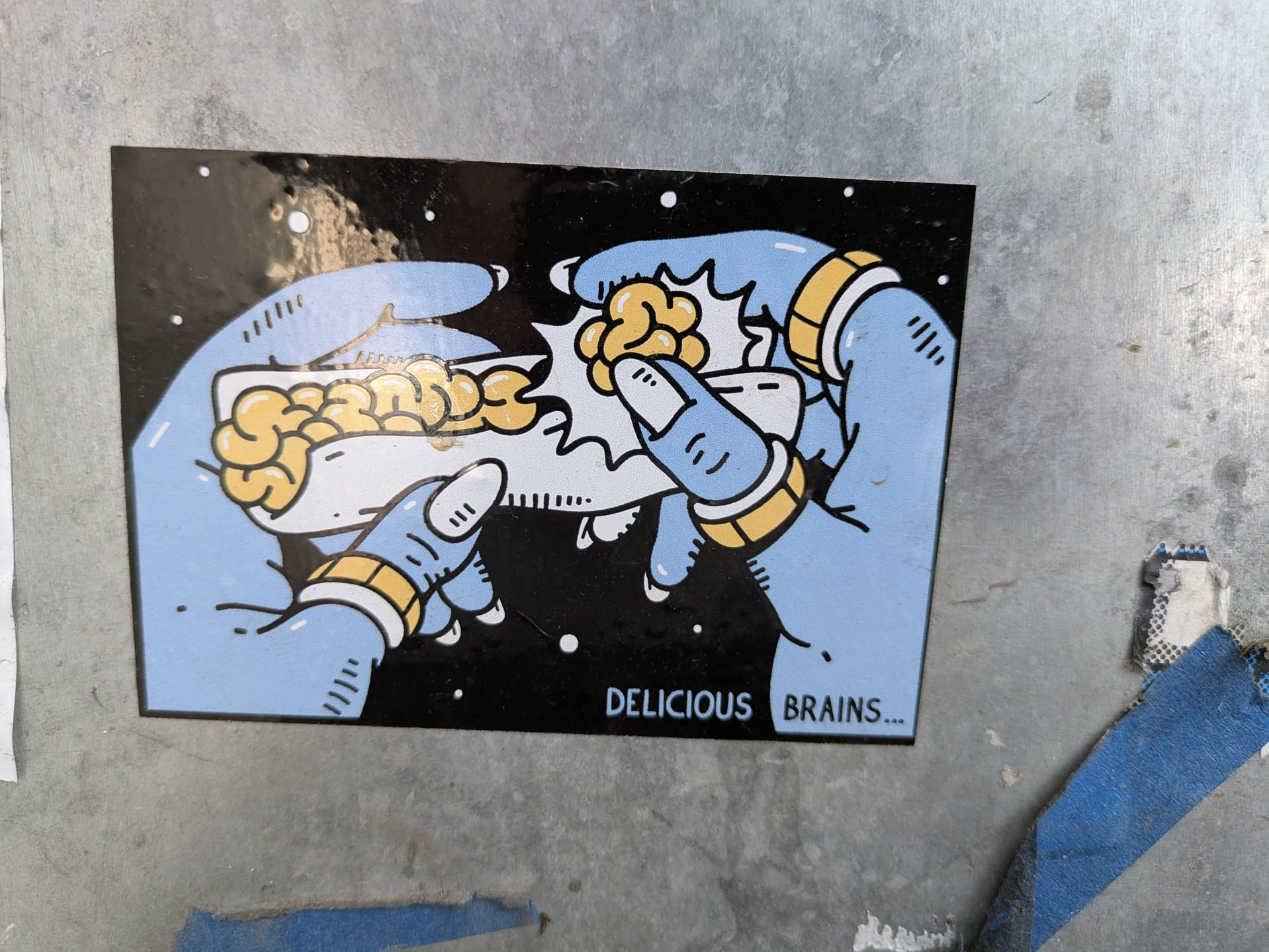 The sticker shows two light blue hands, each adorned with gold rings, preparing a brain-filled taco. The background is black with white dots, resembling space. The text at the bottom reads 'DELICIOUS BRAINS...'.