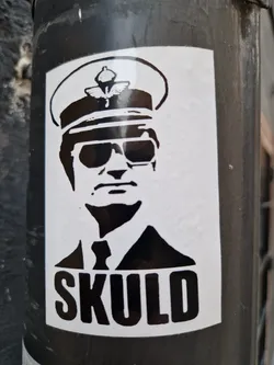 This sticker showcases a minimalist, black and white design of a man resembling a captain, possibly a police officer. The image is simple, yet striking. The word SKULD is placed prominently below the portrait. The style seems to be inspired by stencil art or screen printing. This sticker could be a part of a larger series or a standalone piece. 