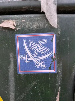 Street sticker The sticker is square with a blue background and a white border, outlined by a thin red line. In the center, two white crossed swords are depicted, with their hilts pointing downwards. Above the swords is a stylized white emblem that resembles wings or a crest, with a prominent white 'K' in the center. The blue background has a subtle pattern of repeating text, which appears to be 'HOCKEY CLUB' in white, though it is difficult to read clearly. The sticker shows some signs of wear and tear, with a small section of the right edge appearing to be peeling or damaged.