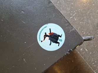 A round sticker featuring a cartoon badger in a red scarf, the number 5, and the text "Ryggsacksäventyret" which translates to "Backpack Adventure" in English. The sticker is applied to a dark gray surface.