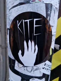 Street sticker Black and white sticker with the word "KITE" stylized with strings attached to a hand. The design is minimalist and impactful, likely representing a concept related to freedom, control, or ambition.
