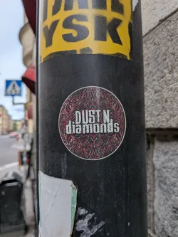 Street sticker A circular sticker featuring a distressed white font reading 'DUST N. diamonds'. The background is a complex, symmetrical red, black, and grey abstract pattern, enclosed by a thin white border.