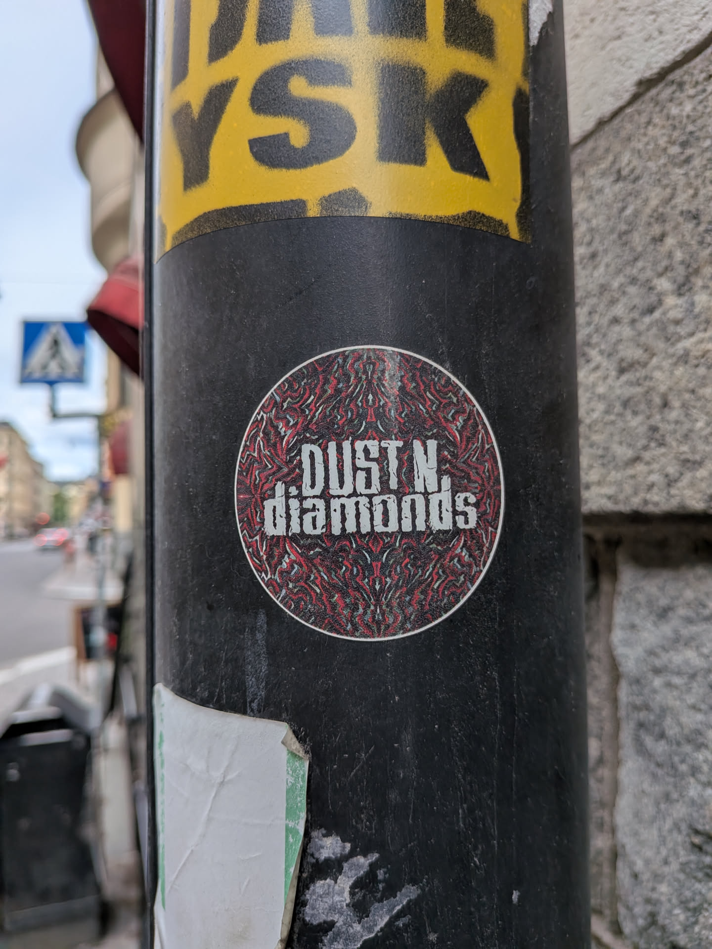 A circular sticker featuring a distressed white font reading 'DUST N. diamonds'. The background is a complex, symmetrical red, black, and grey abstract pattern, enclosed by a thin white border.