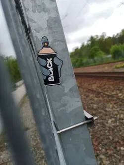 Street sticker The sticker depicts a stylized black spray paint can with a light peach-colored top and a grey nozzle. A grey hand, with four fingers and a thumb, is shown holding the can. The word "BLACK" is written vertically in white capital letters on the side of the can. The entire design is outlined with a thin white border.