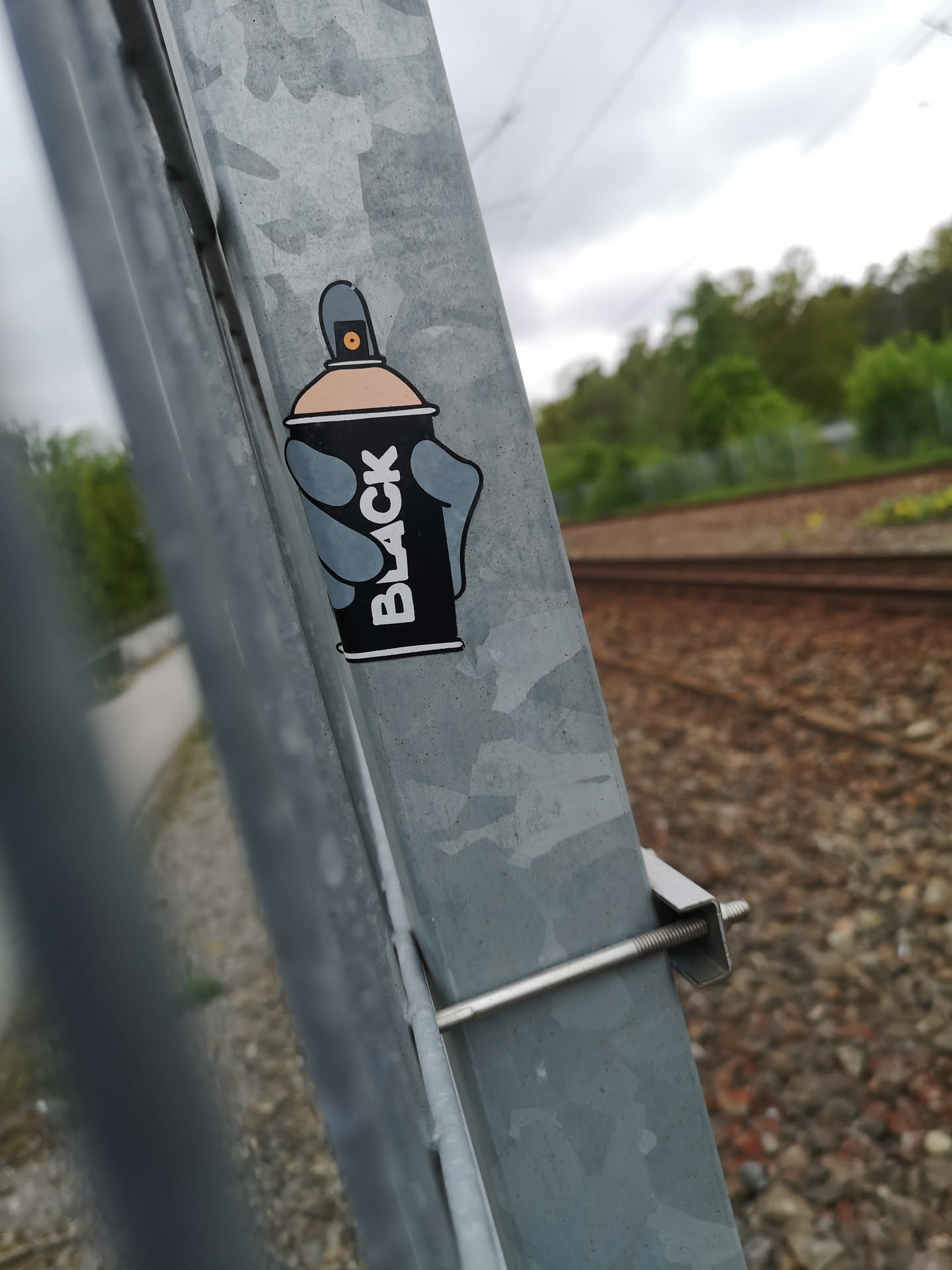 The sticker depicts a stylized black spray paint can with a light peach-colored top and a grey nozzle. A grey hand, with four fingers and a thumb, is shown holding the can. The word "BLACK" is written vertically in white capital letters on the side of the can. The entire design is outlined with a thin white border.