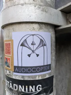 Street sticker A sticker featuring a graphic design of two crossed megaphones within an arched frame. The word 'Audiocopter' is printed below the graphic. 