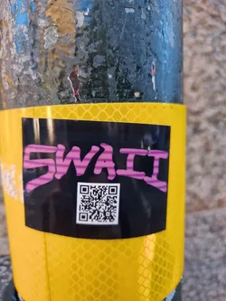 Street sticker A black sticker with the word "SWaii" written in purple and a QR code underneath. The sticker is placed on a yellow reflective surface.