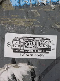 Street sticker The sticker is white with black line art. It depicts a stylized subway train moving from left to right, indicated by motion lines on the right side. The train's front has a rounded top with four circular windows and a windshield. Inside one of the train cars, a cartoon cat's head is visible, with large eyes and whiskers. This cat appears to be saying "UXU" which is written above its head. Another speech bubble to the right of the cat contains the text "THE SABOT CATS" and what appears to be a stylized "A" in a circle. Below the train, the text "UP TO NO GOOD!" is written in a playful, uneven font, with an exclamation mark and two horizontal lines at the end.
