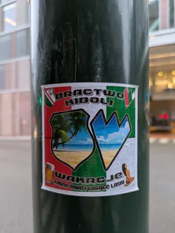 Street sticker The sticker features a shield-like design with a beach scene and a mountain range. It includes the text "BRACTWO KIBOLI" and "WAKACJE zimne PIWO I GORĄCE LASKI". The sticker appears to be related to football fans and vacation theme with cold beer and hot babes.