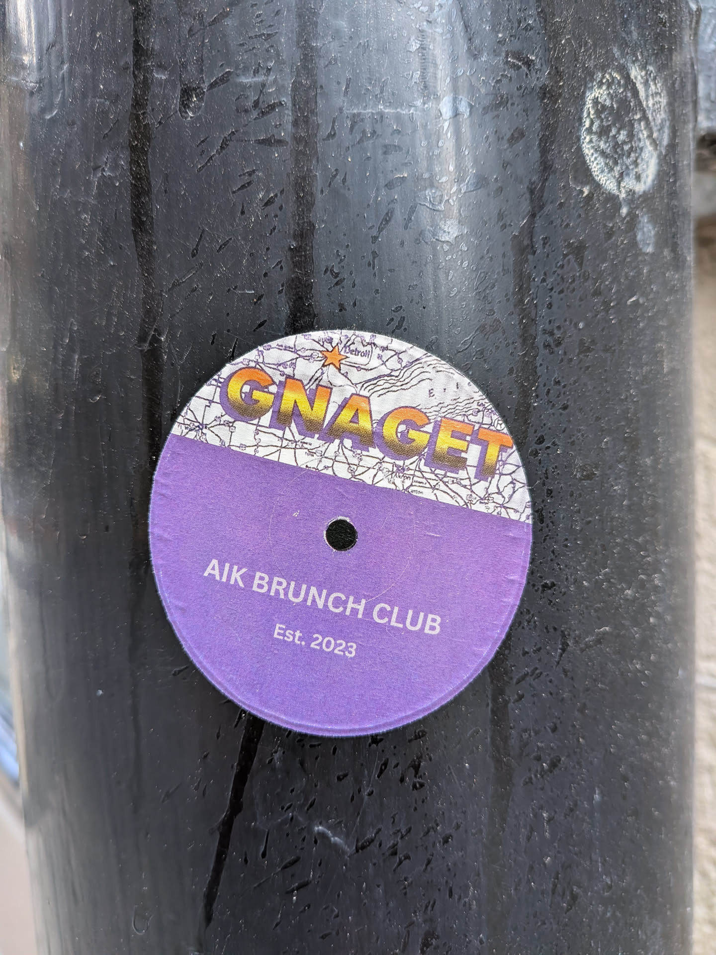 A circular sticker styled like a vinyl record. The top section features a map background with 'GNAGET' in gradient text and a star near 'Detroit'. The bottom section is purple with a center hole, reading 'AIK BRUNCH CLUB Est. 2023' in white.