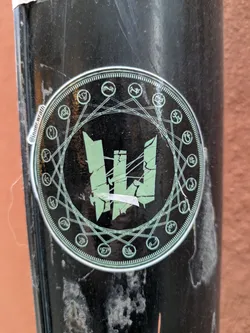 Street sticker A round sticker with a dark background and a central design of a stylized, fractured letter "W." The "W" is surrounded by a circular frame with various symbols and connecting lines, suggestive of occult or esoteric symbolism. The text '@Inner Wrath' is visible on the left side of the sticker.